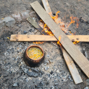 Ein antiker Tontopf mit Suppe steht auf der Glut des Lagerfeuers